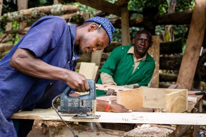 Man using jigsaw to cut plywood, while another man looks on.