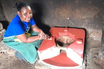 Woman sits over, in preparation of use, a new improved cookstove.