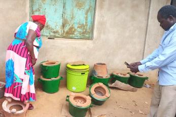 Woman inspects improved cookstoves while man photographs.
