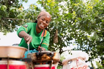 Woman smiling, cooking outside.