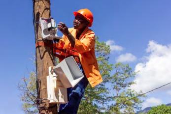 Ugandan working on installing power component on pole.