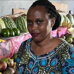 Woman stands smiling, in front of table of fruit.