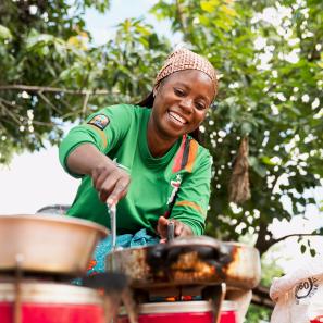 Woman smiling, cooking outside.
