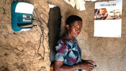 Woman stands in room with solar monitor on the wall, along with a calendar.