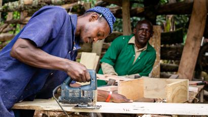 Man using jigsaw to cut plywood, while another man looks on.