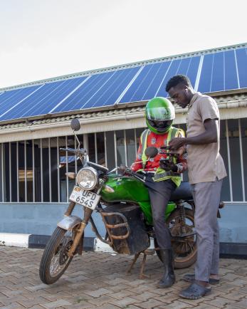 person on motorcycle talking to a man in front of solar panels