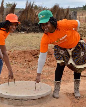 two women pulling on a well cover